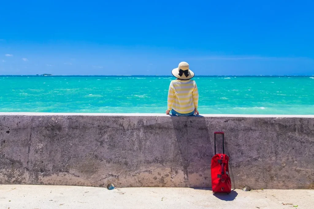 沖縄のビーチに訪れた女性の後ろ姿とキャリーバッグの画像